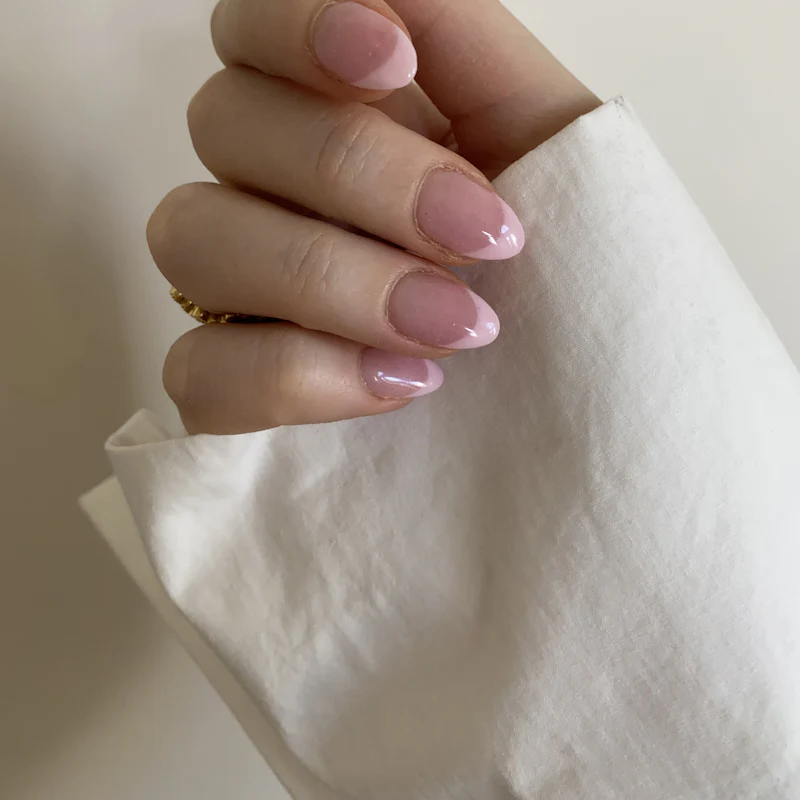 Sheer pink almond nails resting on white linen