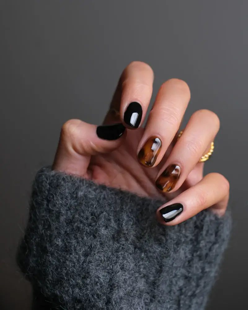 Black and tortoiseshell nail set with a gold ring against a grey knit sleeve