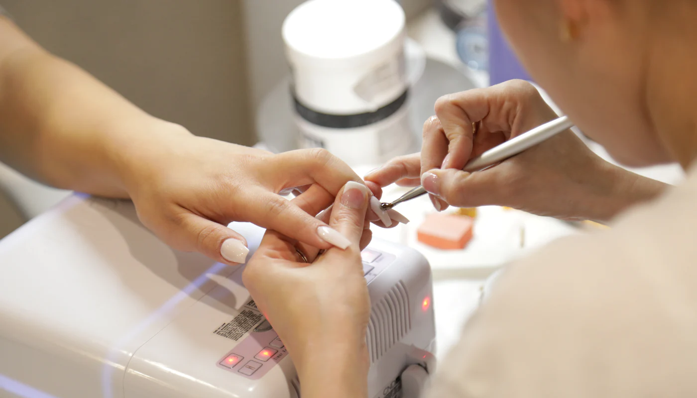 Nail technician carefully filing a client's nails at a bright desk