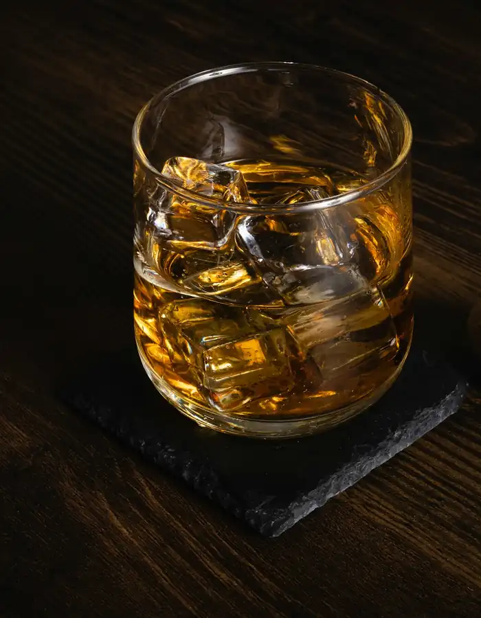 A glass of whisky with ice on a dark wooden table