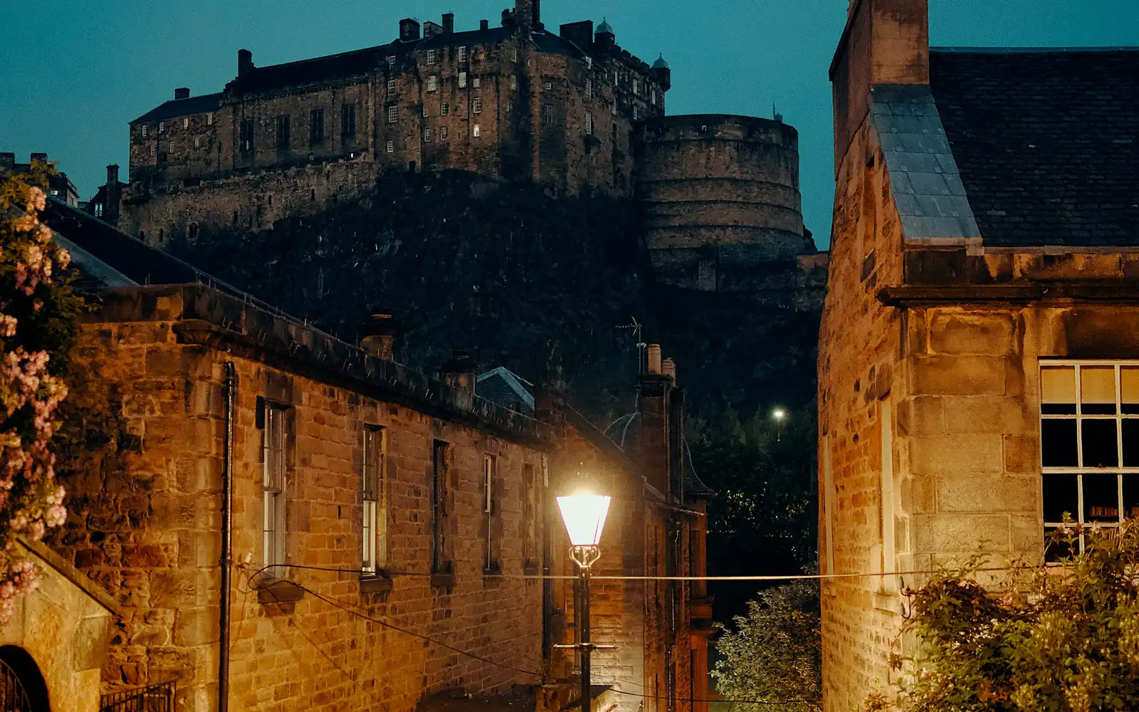 Edinburgh Castle rising above old stone tenements and a lamplit street at dusk
