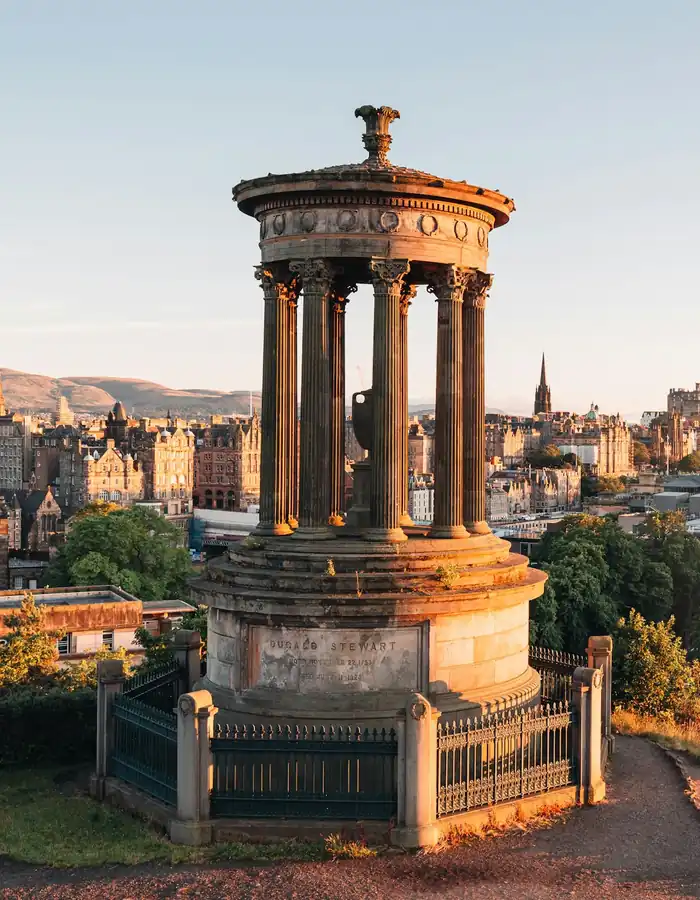 A circular classical monument on a hill overlooking the city skyline at golden hour