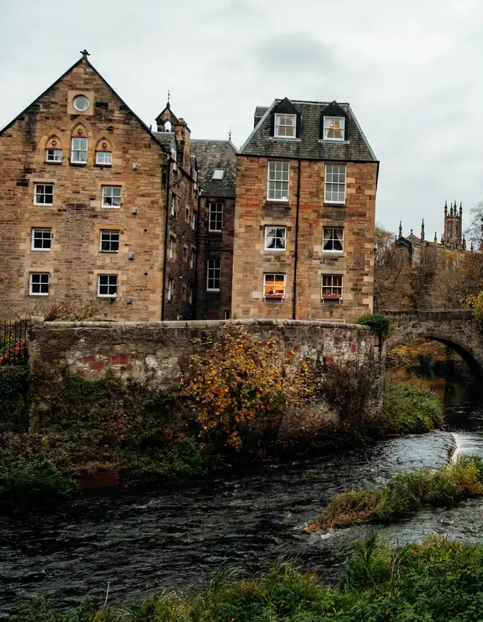 Old stone mill buildings and an arched bridge over a river among autumn trees
