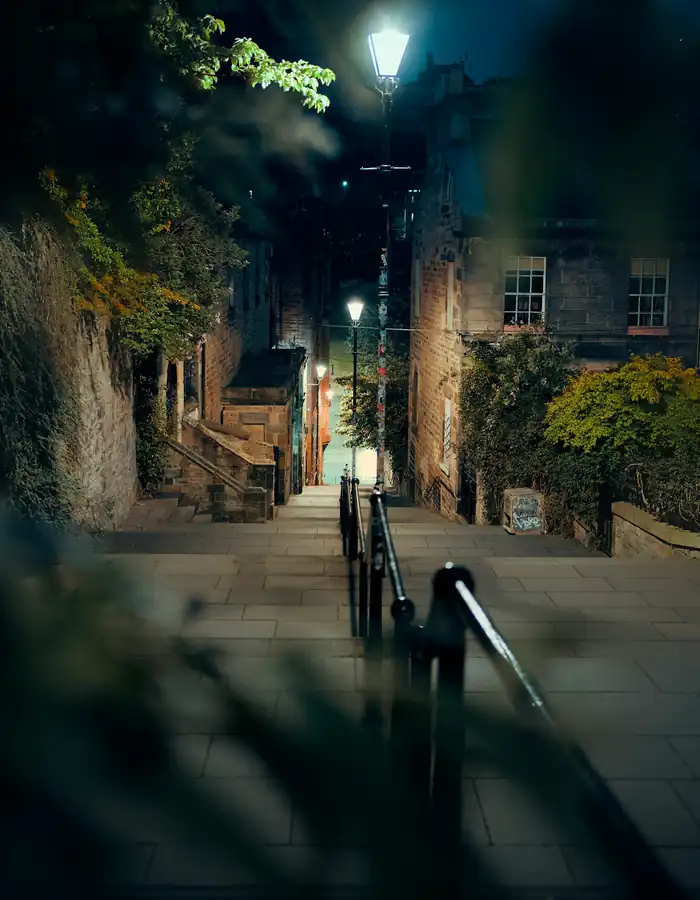 A narrow stepped close between old stone buildings, lit by street lamps at night