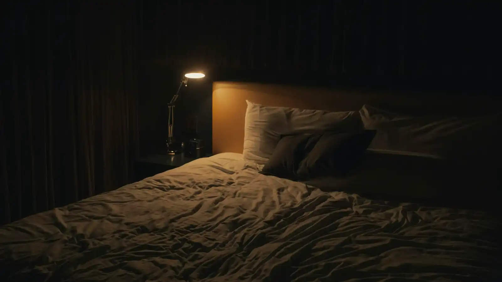 A dimly lit bedroom at night with a single reading lamp beside the bed