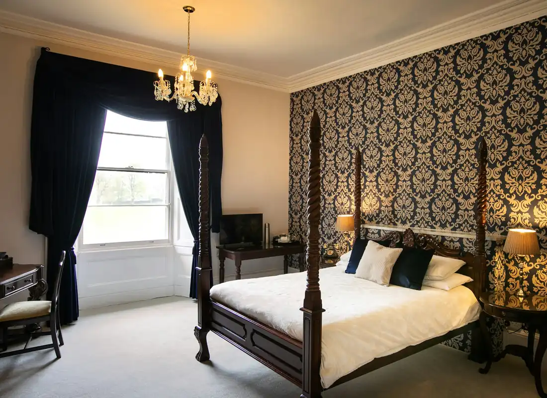 A grand bedroom with a dark wood four-poster bed, damask wallpaper and a chandelier