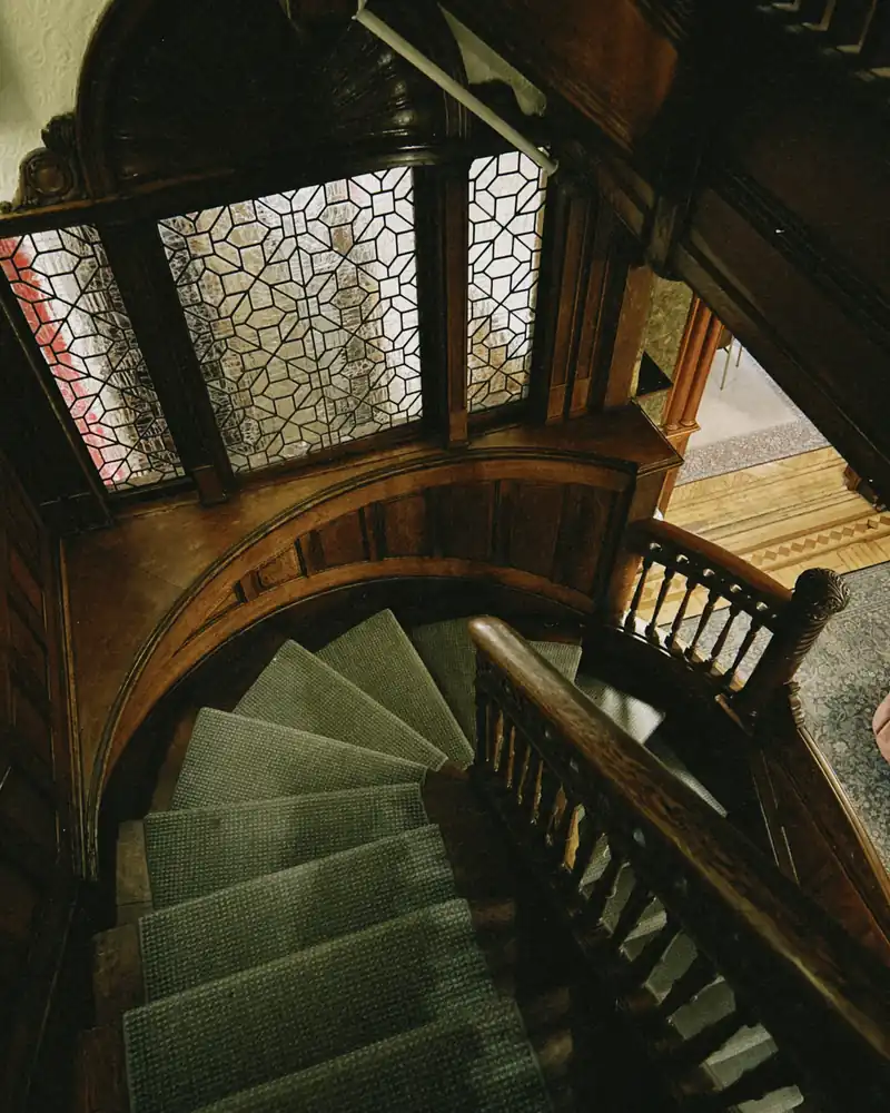 Looking down a curving Victorian wooden staircase beneath a patterned glass cupola