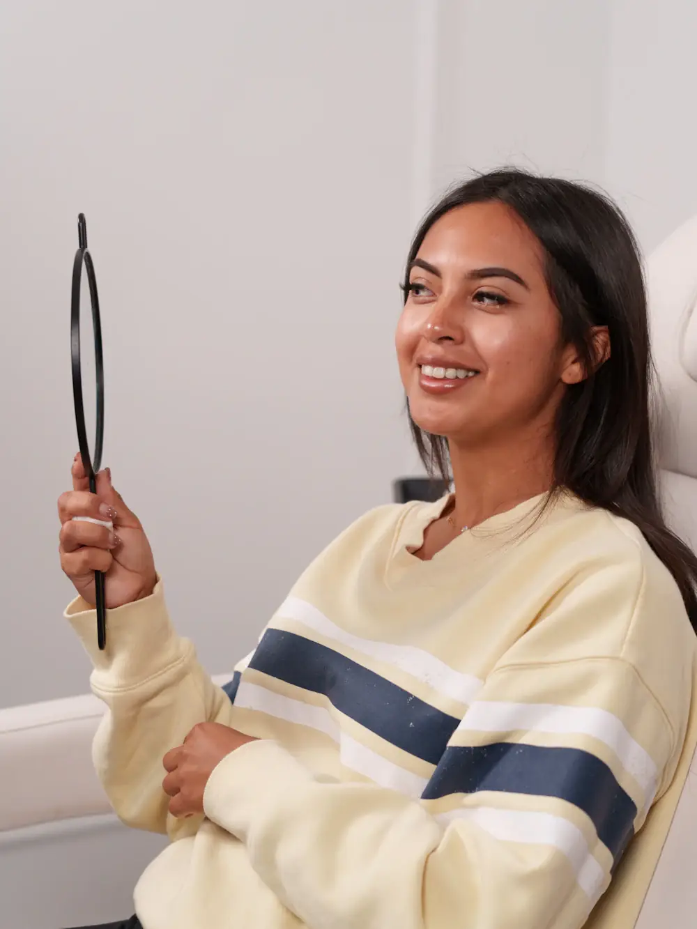 A smiling woman checking her teeth in a hand mirror after a dental visit