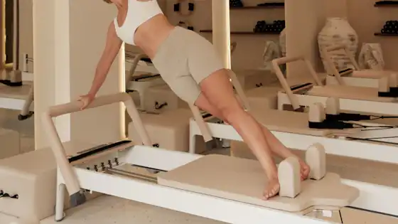 Client in a long lunge on a reformer, studio mirrors behind