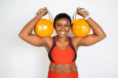 Portrait of coach Ada Okafor smiling with two orange kettlebells on her shoulders