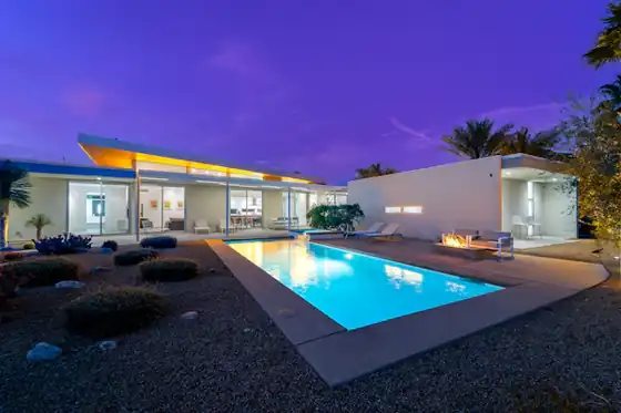 Low pavilion home with a glowing pool and fire pit under a violet evening sky