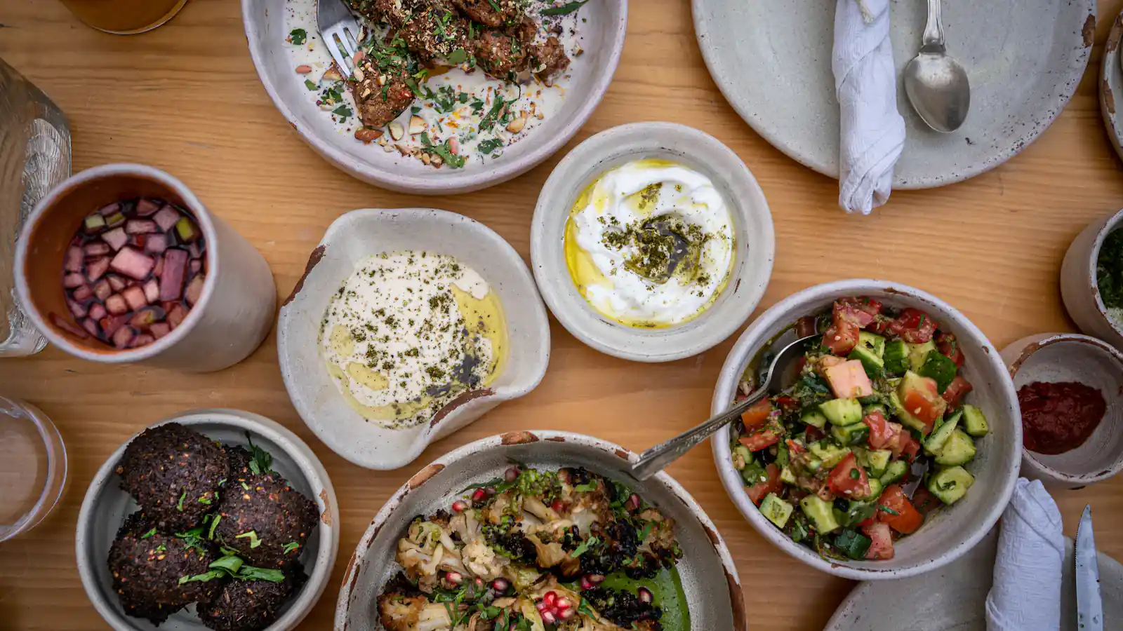 Overhead view of a wooden table covered with mezze: labneh, hummus, herb salad and grilled vegetables
