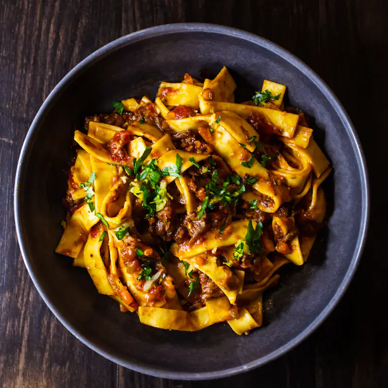 Pappardelle with ragù and herbs in a dark bowl