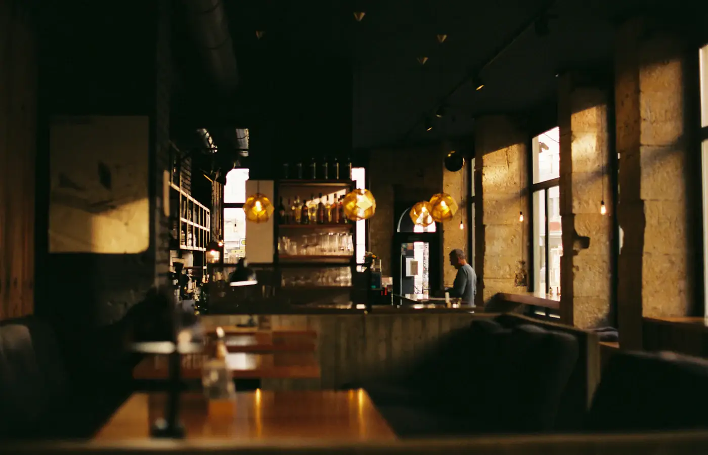 Dim, warm dining room with a long bar and pendant lights