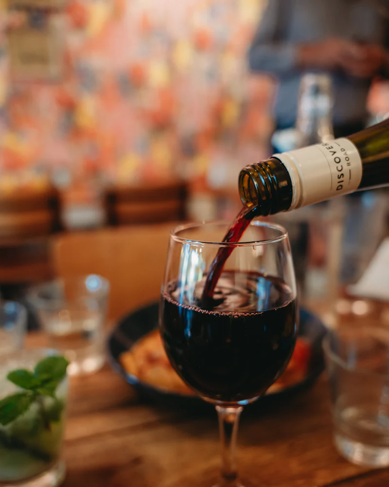Red wine poured from a bottle into a glass on a busy restaurant table